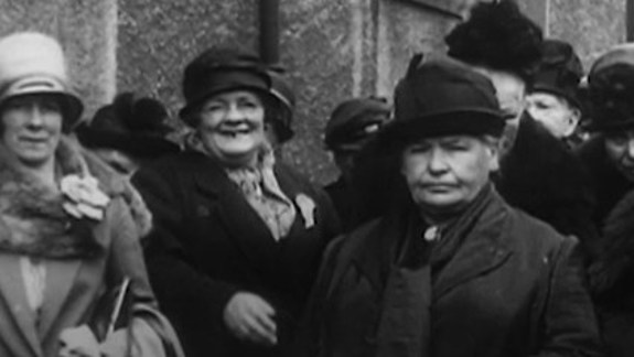 A vintage black and white photo of women in coats standing closely together.