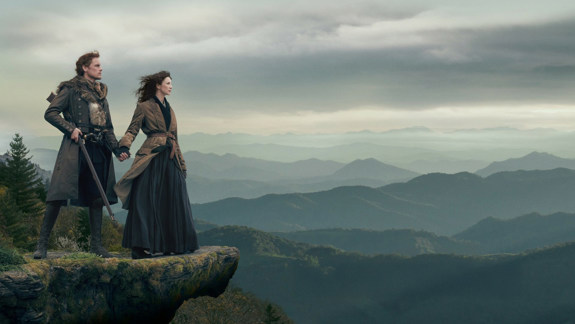 Still from the film 'Outlander'. Two people stand on a rocky outcrop overlooking a mountainous landscape.
