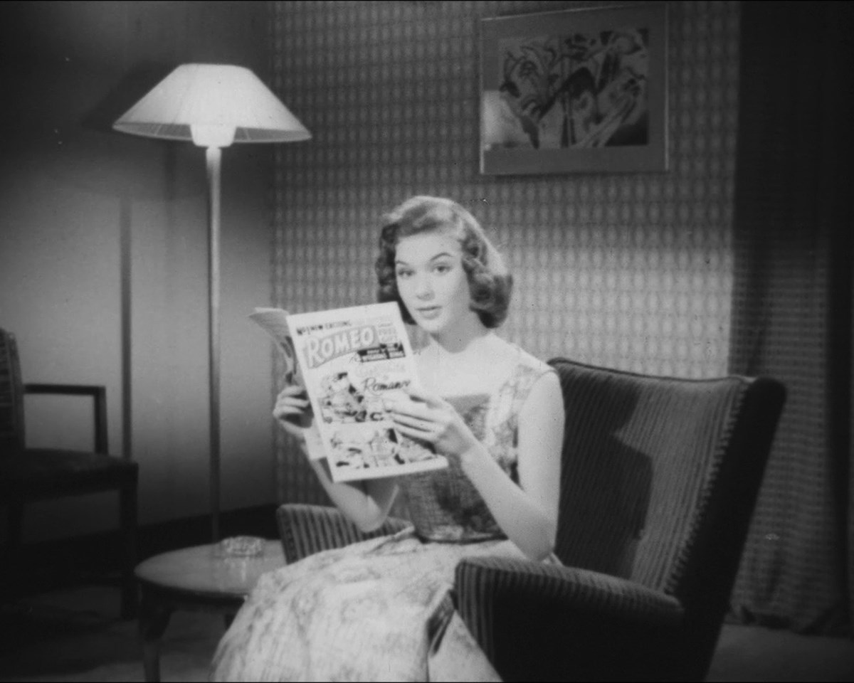 Black and white photo of a woman sitting in an armchair reading a magazine.