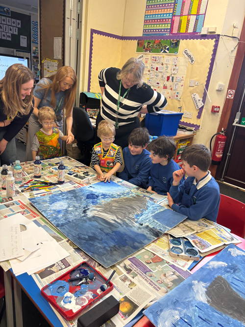 Children gathered around a table with teachers painting stormy weather.