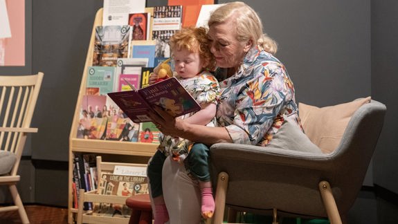 A baby sitting on an adult's lap while they read them a story.