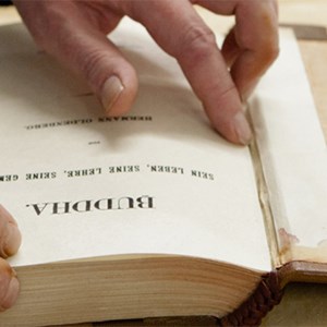 A photo of someone bookbinding, it is focused on their hands. The book plate is open and a weight holds down the book cover which has just been glued.