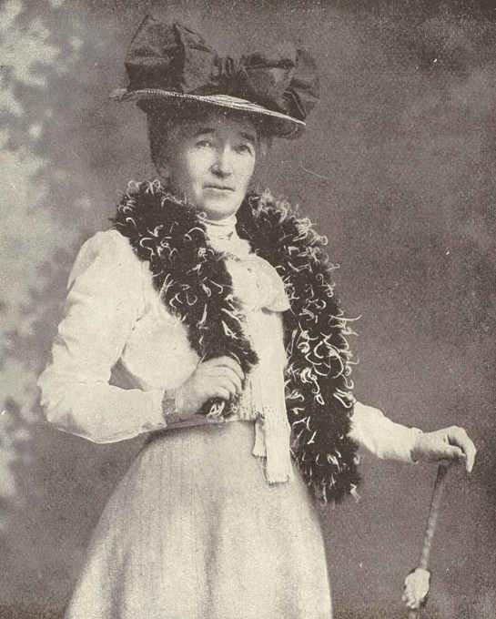 A woman standing wearing a hat with a large bow on it