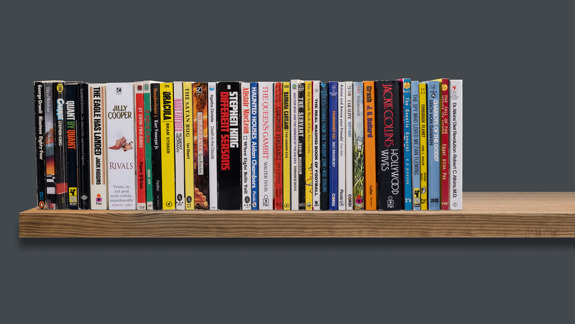 Several paperback books sitting on a shelf.