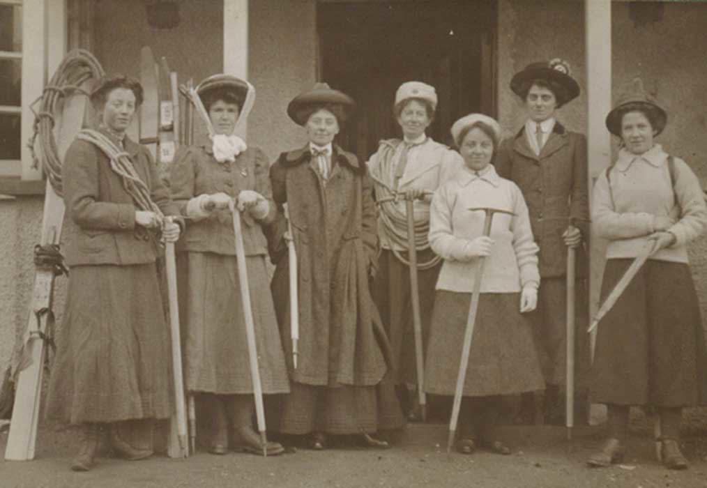 Seven women holding or adorned with various forms of 20th century climbing equipment