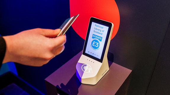 A hand holding out a debit card to tap a machine to donate