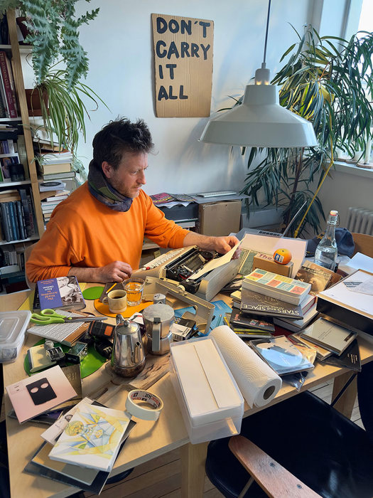 A man at a typewriter on a table in an eclectic studio.