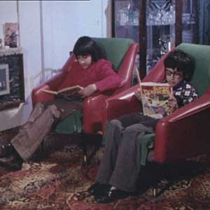 Two young boys sitting in armchairs reading books, one of which is title 'Super TV Heroes'