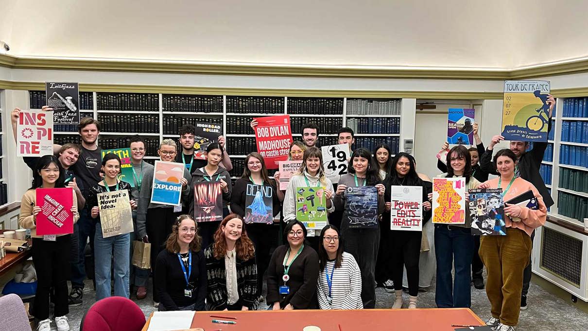 A group of people stand holding posters in a room lined with books.