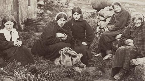 Vintage black and white photo of a family sitting together, huddled next to a croft.