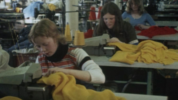 Three people working in a Twomax knitwear factory sewing yellow jumpers.