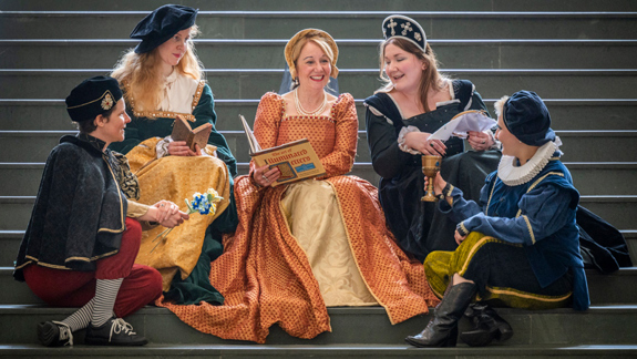 Five people dressed up in Renaissance-era clothing sitting on the main steps of the Library.