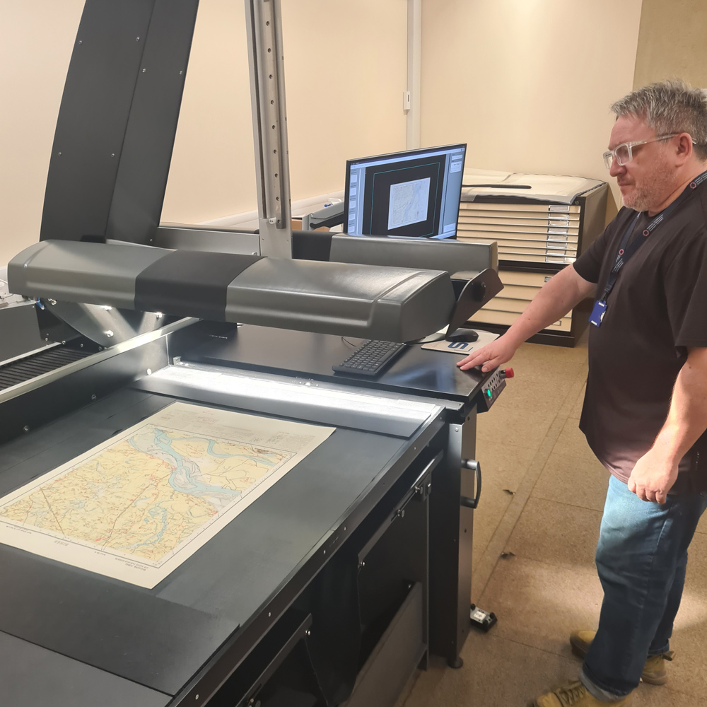A man standing in front of a large digitising machine that is scanning a map.