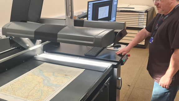 A man standing in front of a large digitising machine that is scanning a map.