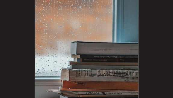 A stack of books in front of a window with rain on it.