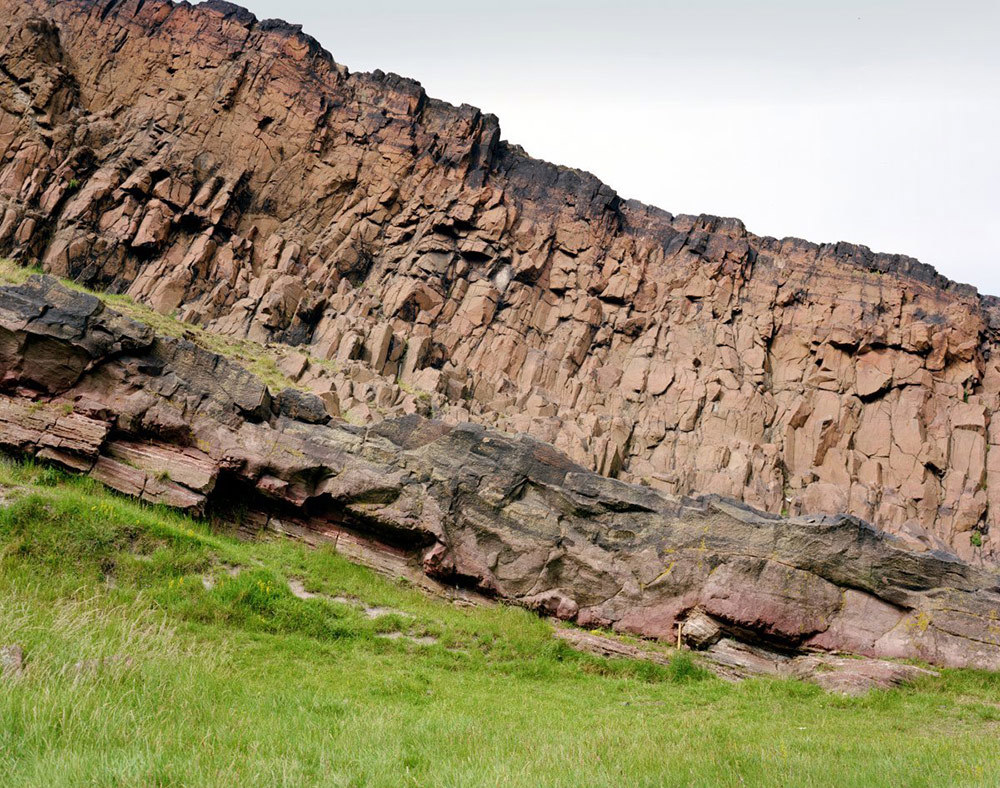 A photo of the Salisbury Crags in Edinburgh. A Rocky cliffside with grass below.