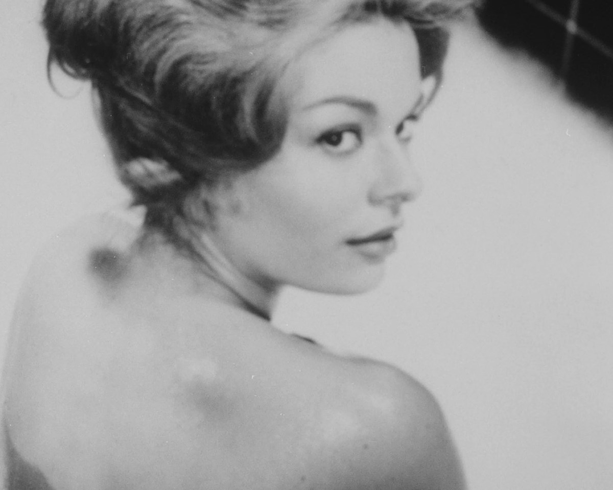 Black and white photo of of a woman looking over her bare shoulder.