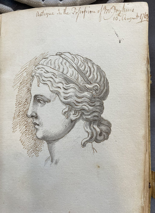 A detailed ink and pencil study of the back and side of a sculpted head with intricately curled hair, drawn on an aged notebook page with handwritten text at the top.