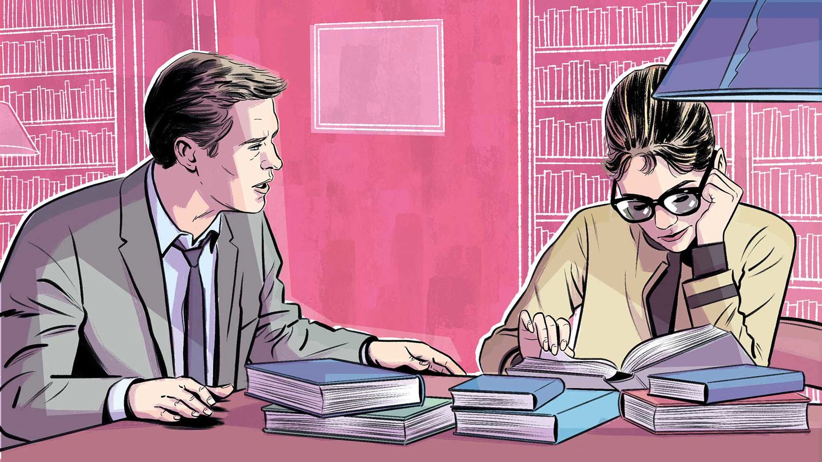 A man and a woman are seated at a desk covered in books in a library. The man is speaking to the woman but she is looking down, reading a book.