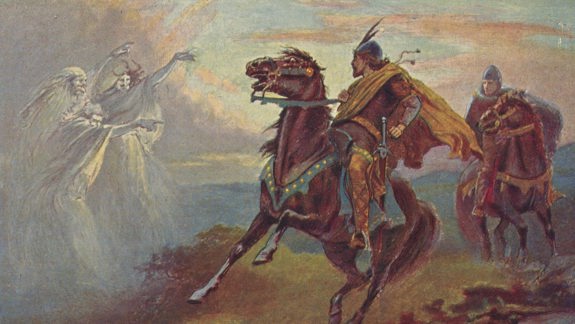 A scene from 'Macbeth' with three witches raising their arms at Macbeth who is riding a horse.