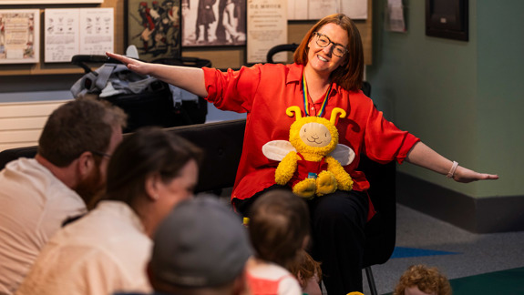 An adult with a bookbug toy in their lap facing a group of children and adults.