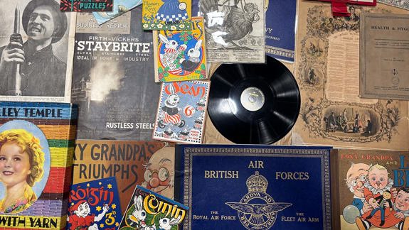 A collection of vintage items including comic books ("Pip," "Roisin," "Percy"), a vinyl record, a Shirley Temple book, "British Air Forces," and a "Moscow News" newspaper, all arranged together with other printed materials.