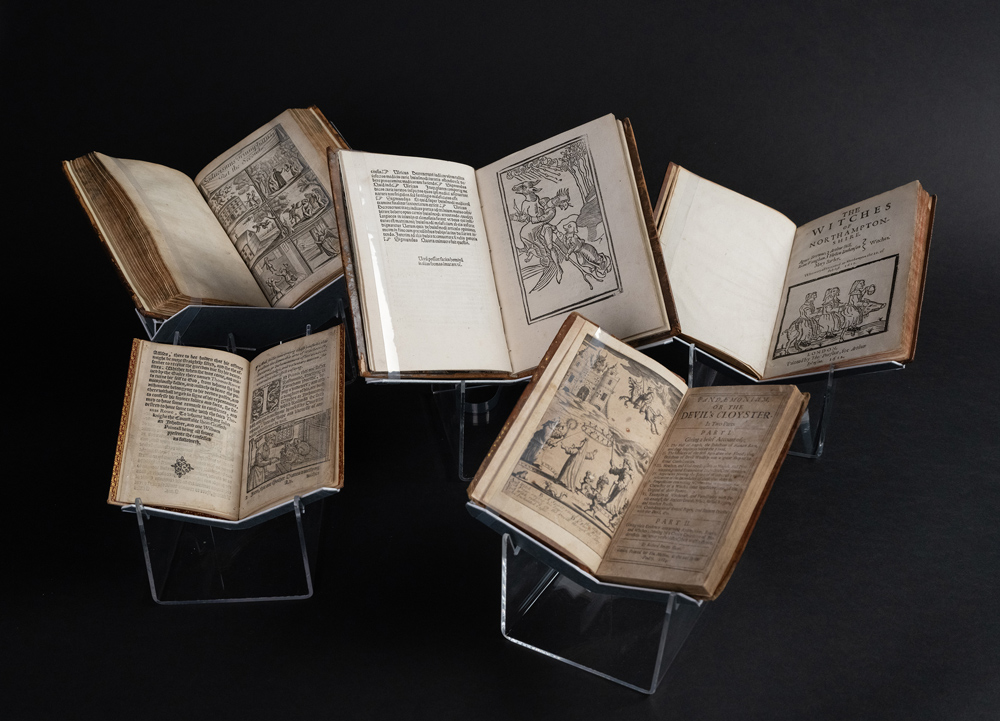 Five old books on display showing early depictions of witches.