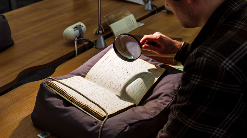 A person looking at a manuscript with a magnifying glass.