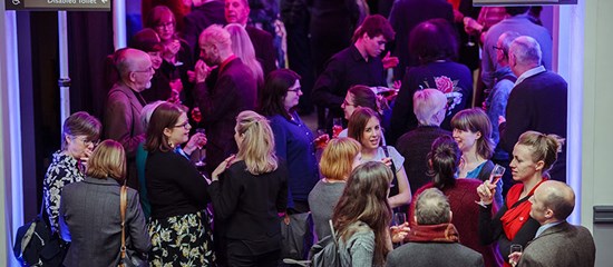 A large crowd of people are standing talking in the foyer of the National Library of Scotland.