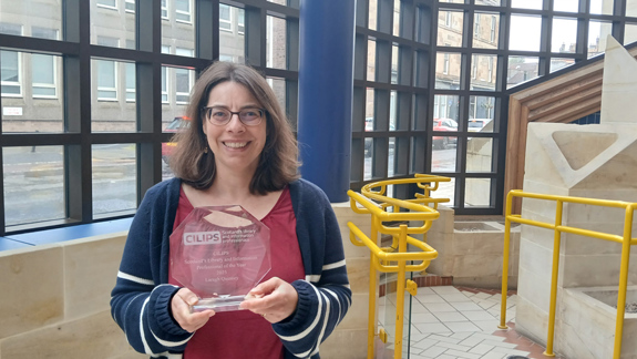 Laragh Quinney stands in the foyer of a building holding her CILIPS trophy.