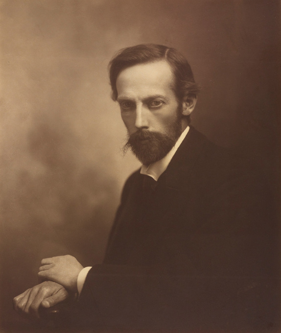 An old black and white photo of a man with a beard in a suit sitting.