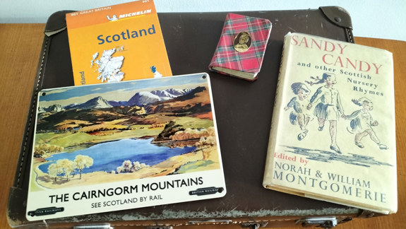 Several books related to Scotland on top of a suitcase.