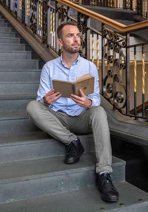 Shane Strachan sitting on steps holding a book.