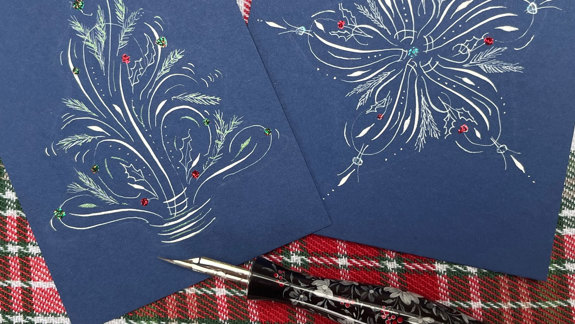Two cards with festive calligraphy on them and a calligraphy pen.