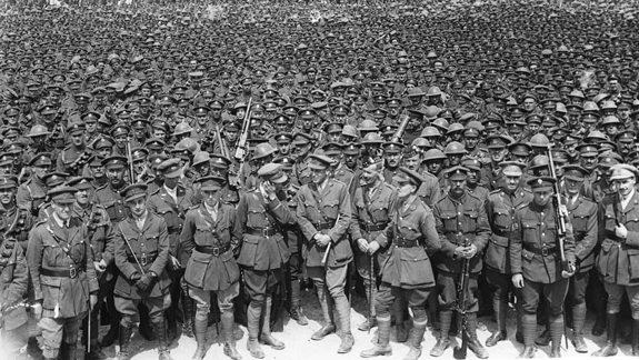 A large group of soldiers in uniform, standing closely together in rows. The soldiers are wearing helmets and carrying rifles.