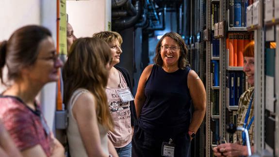 A group of teachers stand among the library stacks.