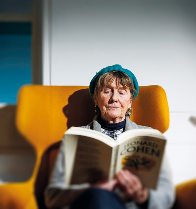 A woman sitting in a chair reading a book about Leonard Cohen.
