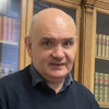 A man's head and shoulders in front of a bookcase.
