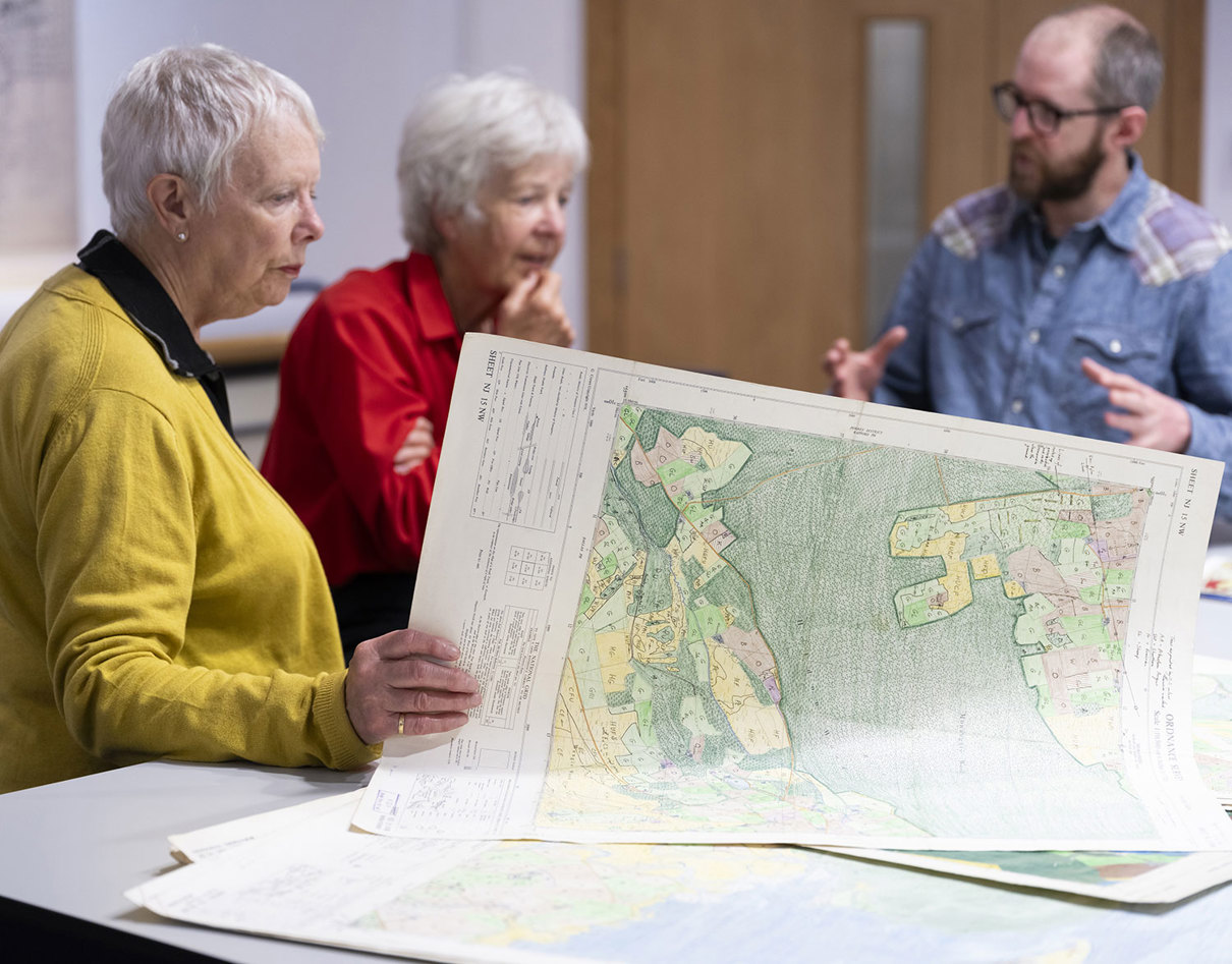 Three adults standing around a table with maps on it.