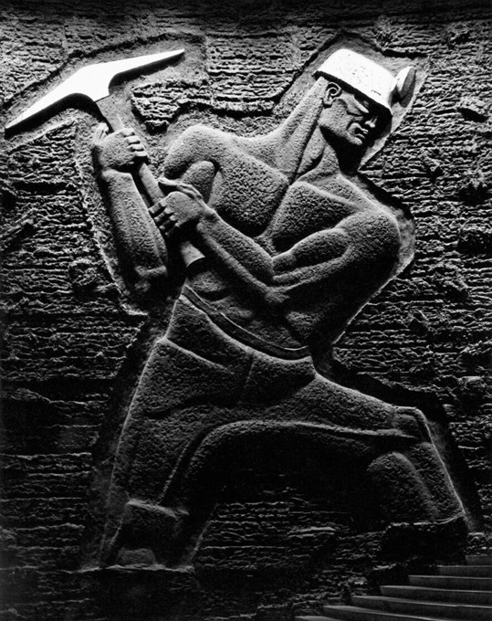 A carving of a man swinging a pickaxe and wearing a helmet with a torch.
