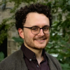 Head and shoulders of a man with curly hair and glasses.
