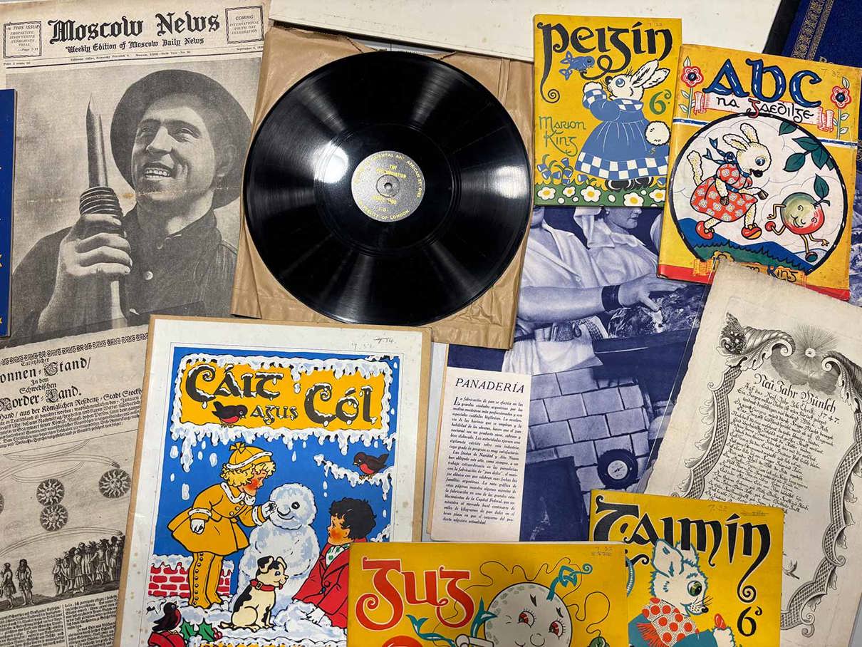 A collection of vintage items including a vinyl record, illustrated children's books with titles like Pejsin, ABC na zabojisce, and Zamin, along with old newspapers such as the Moscow News.