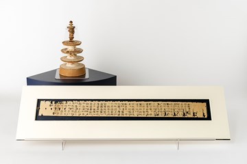Miniature wooden pagoda next to a scroll with ancient text